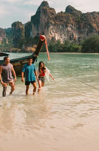 A group wading ashore from a traditional long-tail boat on a beach in Krabi - Contiki Southern Thailand: Khao Sok & Krabi Tour
