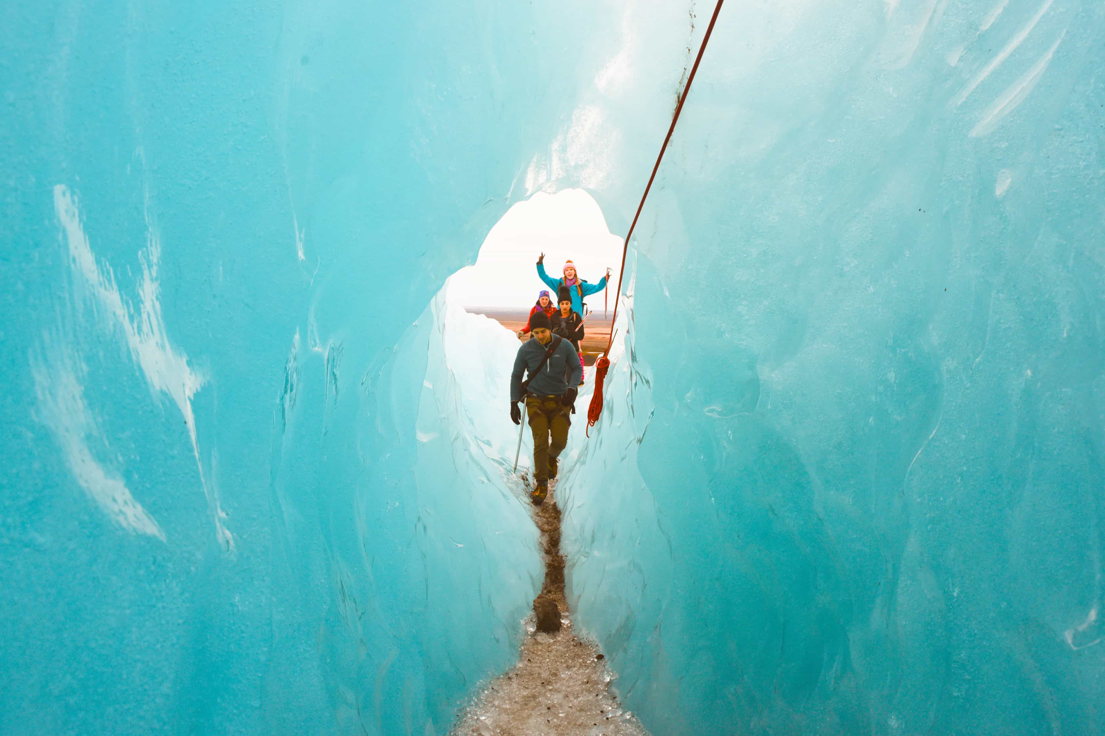 Travellers roped together walking through a glowing blue ice cave in Iceland.