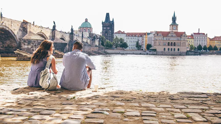 Travellers sat at the waters edge in front of Charles Bridge in Prague, Czech Republic