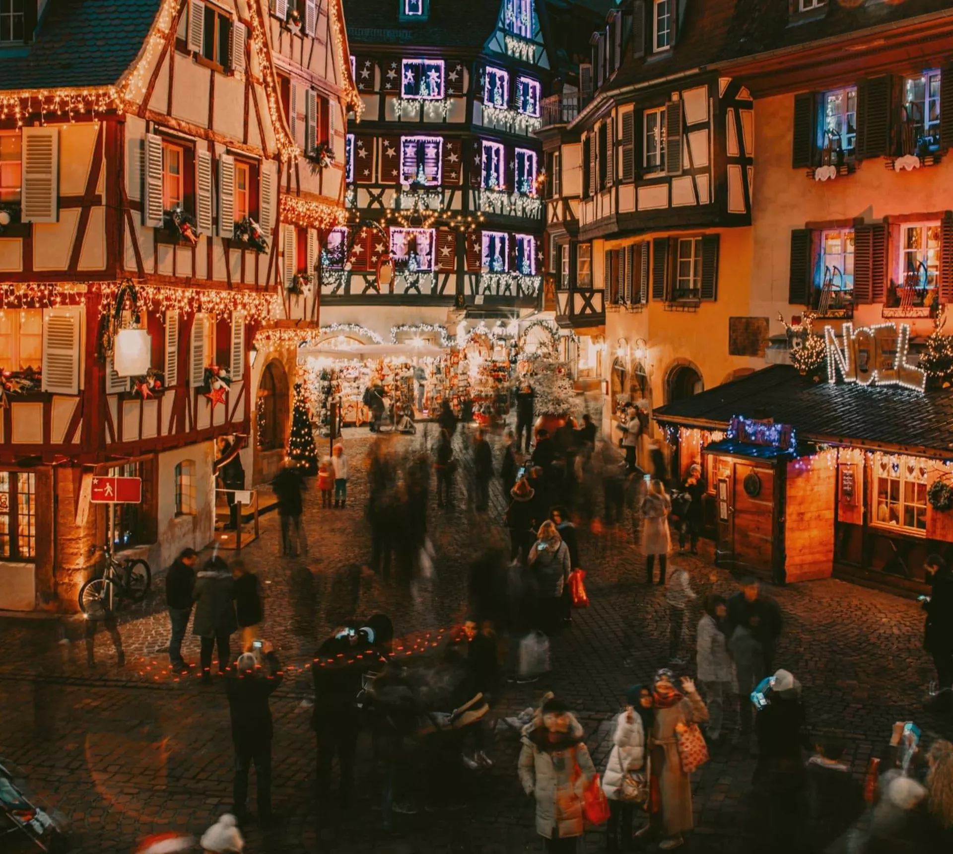 Travellers explore a festive Christmas market surrounded by illuminated half-timbered buildings in France on the Contiki French Christmas Markets Tour