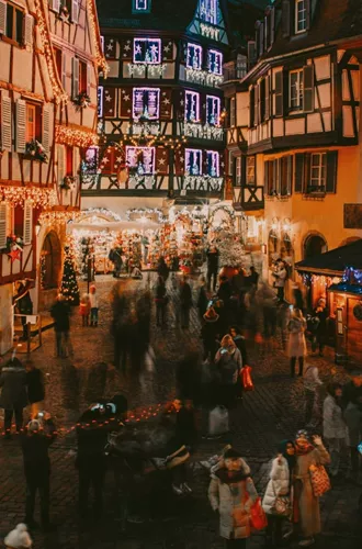 Travellers explore a festive Christmas market surrounded by illuminated half-timbered buildings in France on the Contiki French Christmas Markets Tour