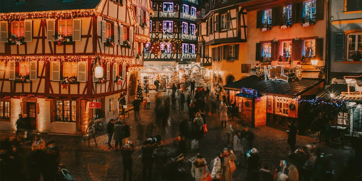 Travellers explore a festive Christmas market surrounded by illuminated half-timbered buildings in France on the Contiki French Christmas Markets Tour