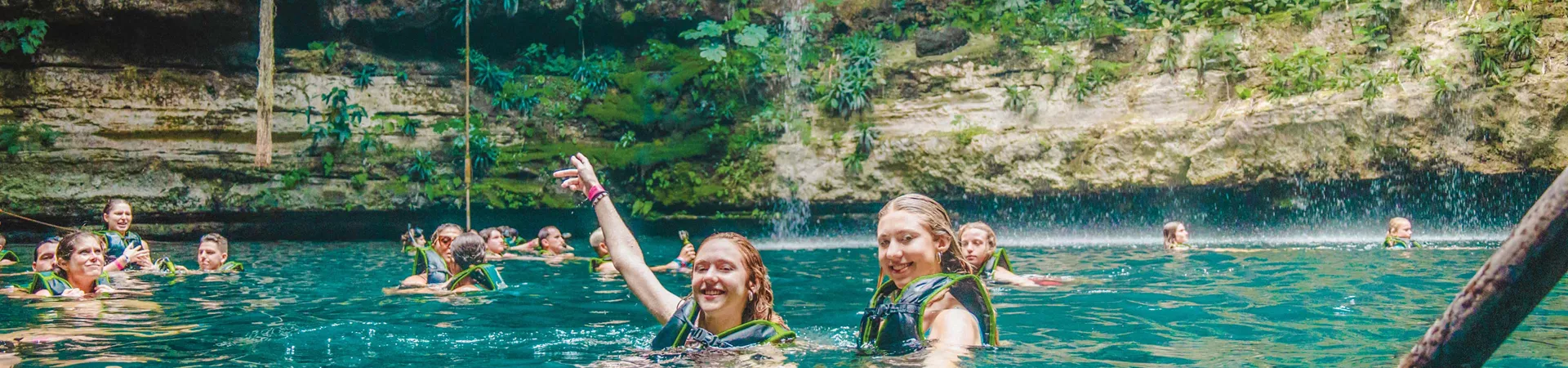 Two Women Swimming In A Natural Pool With A Group Of People