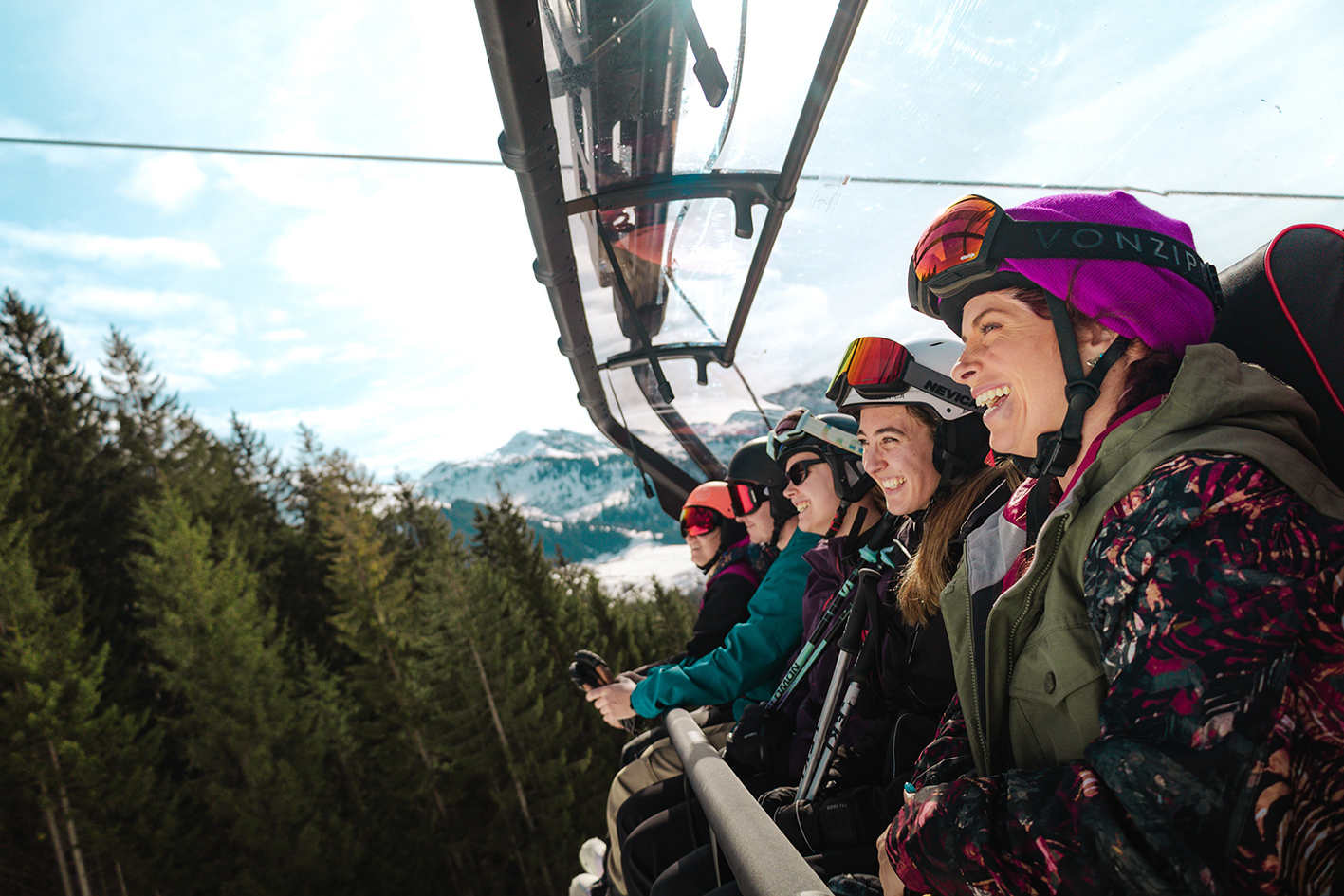 Five travellers sitting on a ski lift with trees and snow topped mountains in the background in Hopfgarten im Brixental, Austria