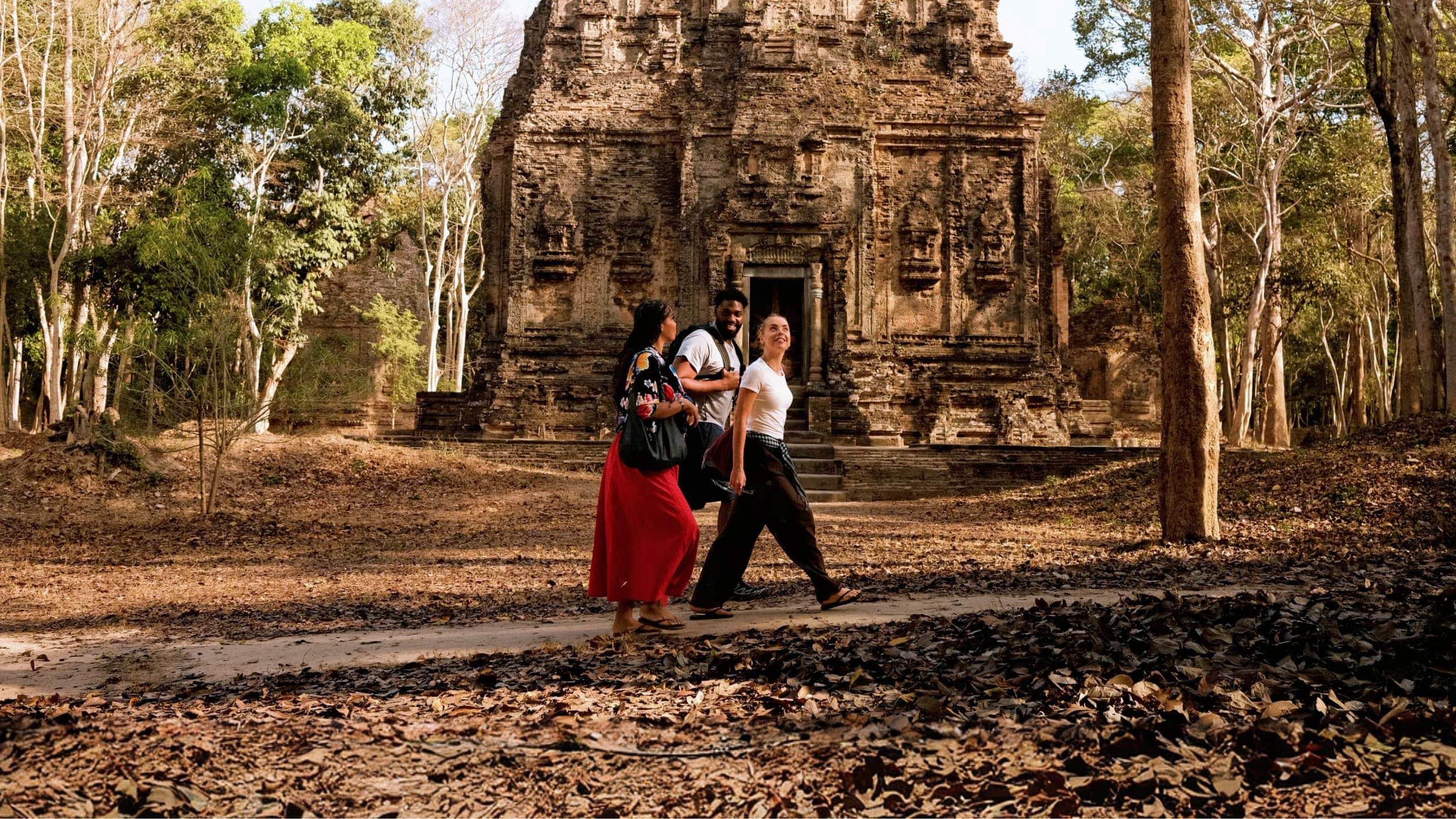 Young travellers walking past an ancient Khmer stone temple in the Angkor Archaeological Park Siem Reap Cambodia - Contiki Cambodia Tour