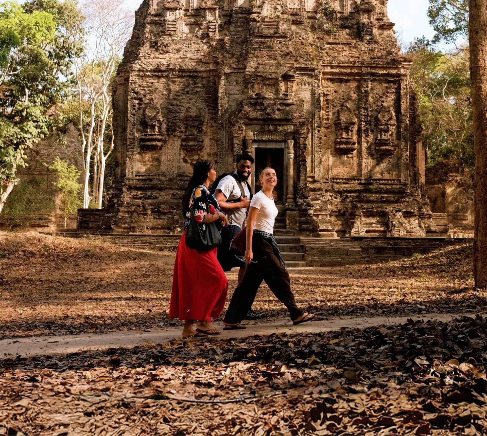 Young travellers walking past an ancient Khmer stone temple in the Angkor Archaeological Park Siem Reap Cambodia - Contiki Cambodia Tour
