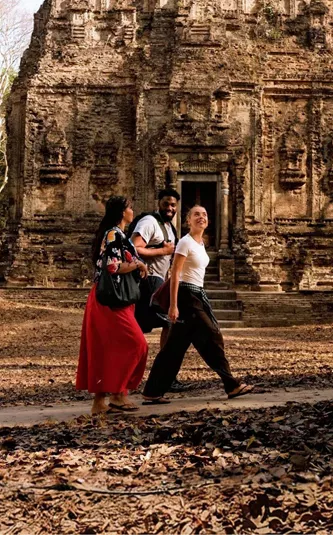 Young travellers walking past an ancient Khmer stone temple in the Angkor Archaeological Park Siem Reap Cambodia - Contiki Cambodia Tour