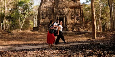 Young travellers walking past an ancient Khmer stone temple in the Angkor Archaeological Park Siem Reap Cambodia - Contiki South East Asia Tour