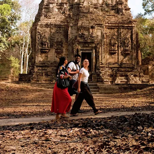 Young travellers walking past an ancient Khmer stone temple in the Angkor Archaeological Park Siem Reap Cambodia - Contiki Cambodia Tour