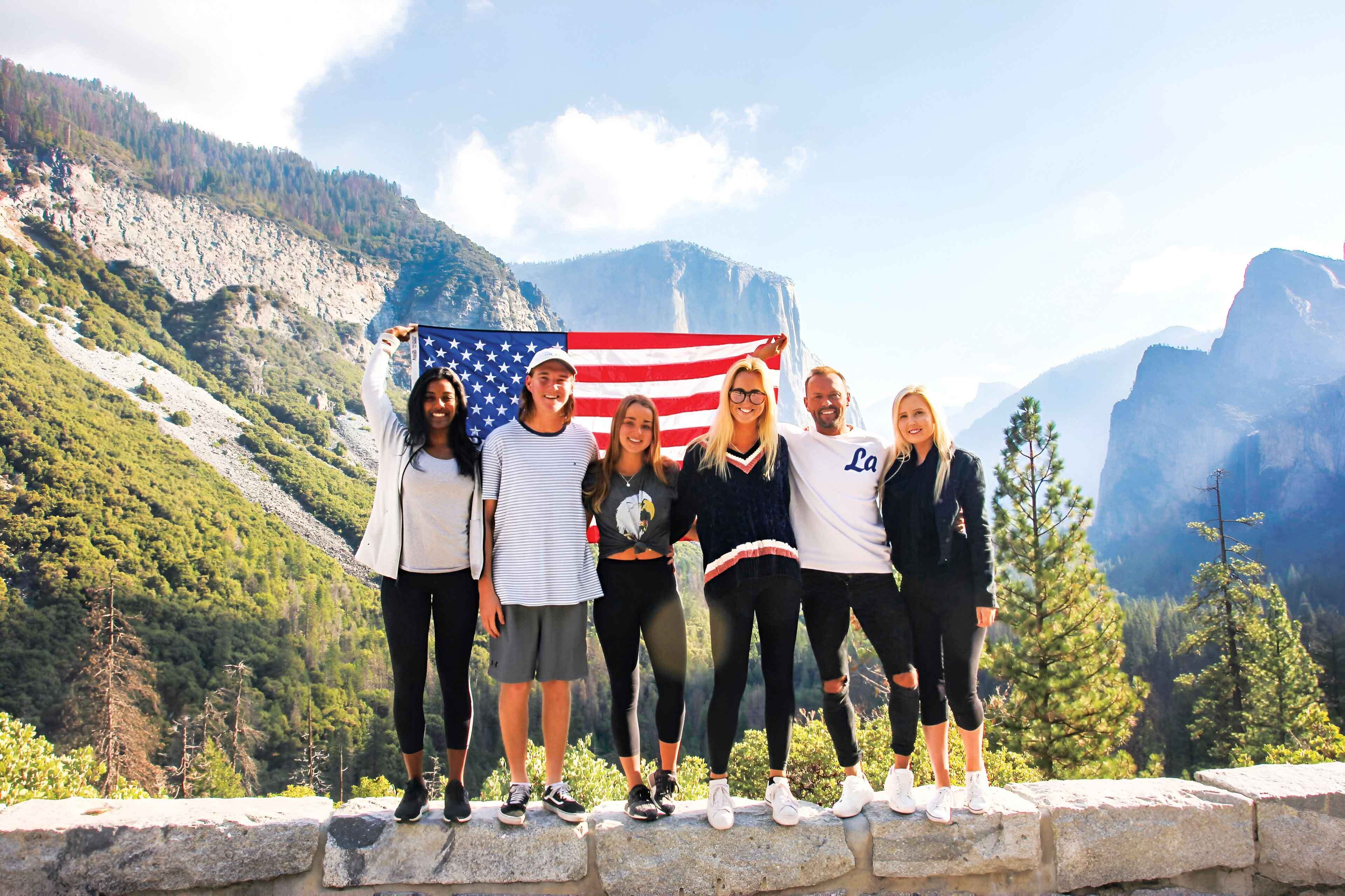 Group Of Young Travelers In Yosemite National Park With Usa Flag