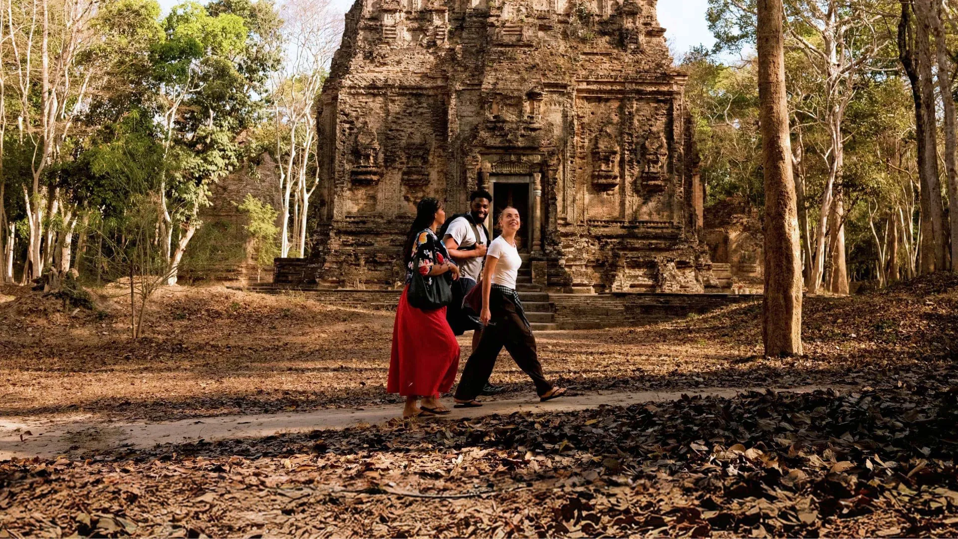 Young travellers walking past an ancient Khmer stone temple in the Angkor Archaeological Park Siem Reap Cambodia - Contiki South East Asia Tour
