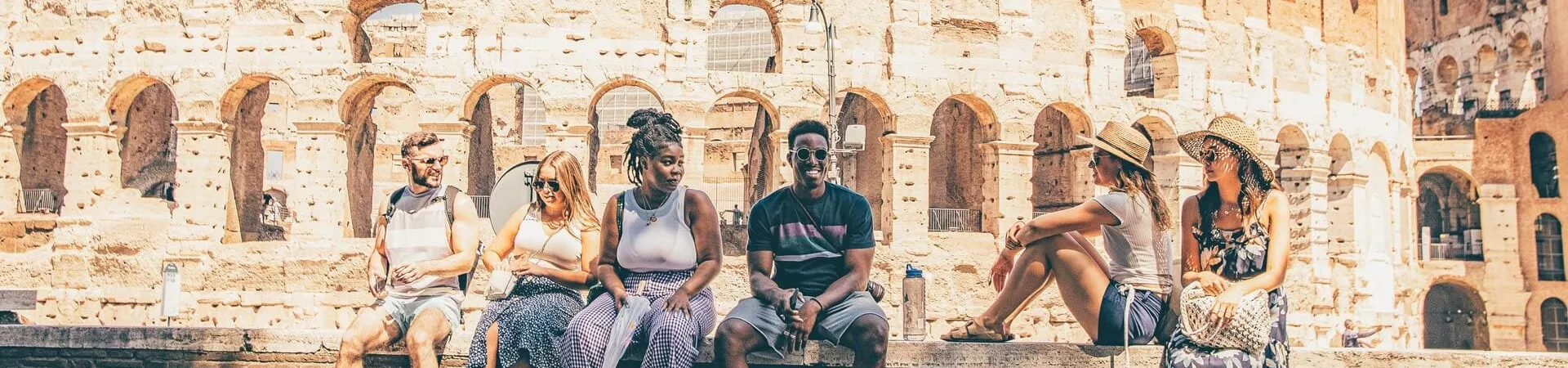 A group of travellers sitting on a wall in front of Collosseum in Rome