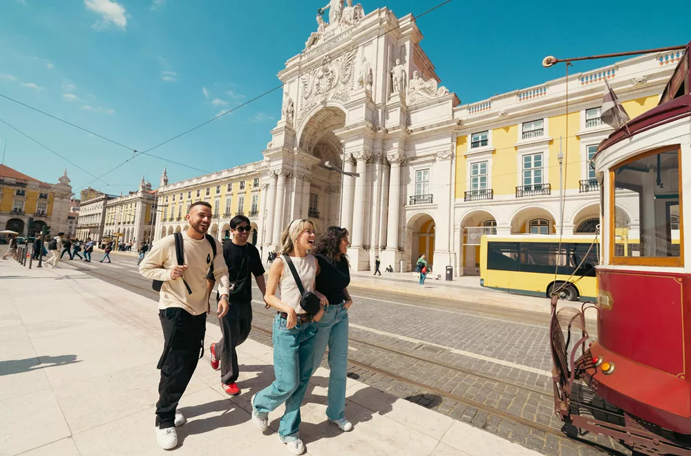 Friends exploring Praça do Comércio in Lisbon with the historic yellow tram on a sunny day in Portugal.