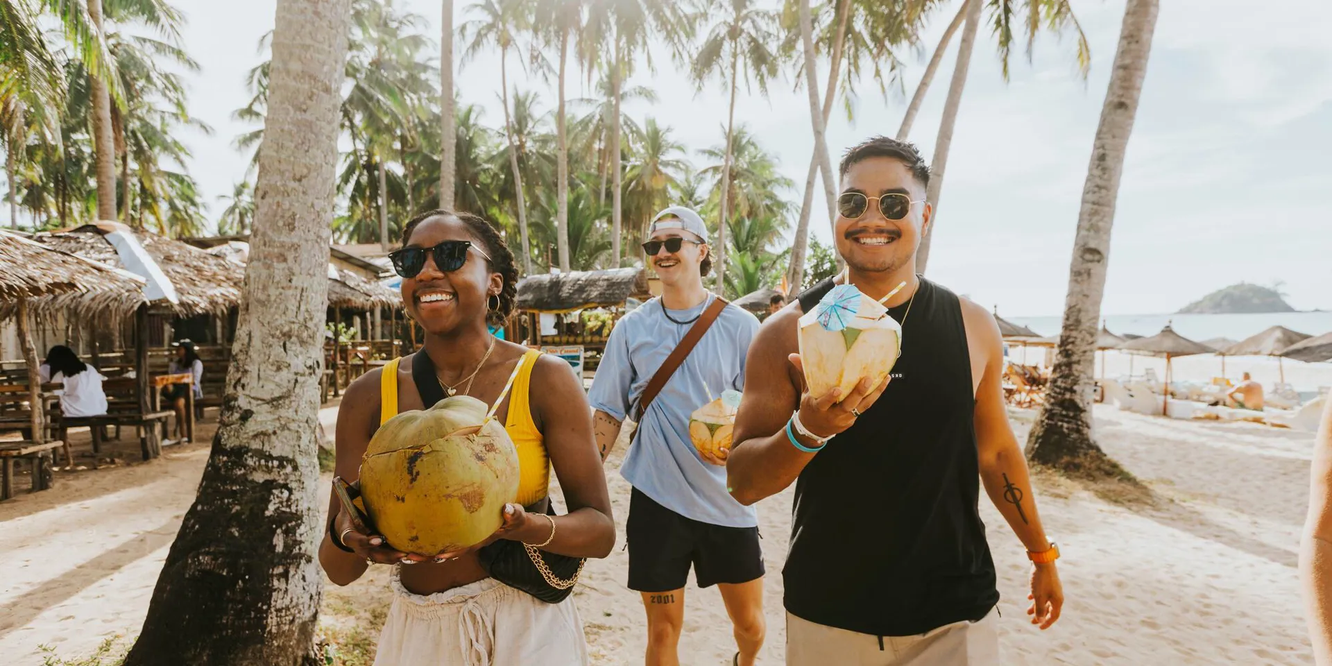 People walking down a beach holding coconuts