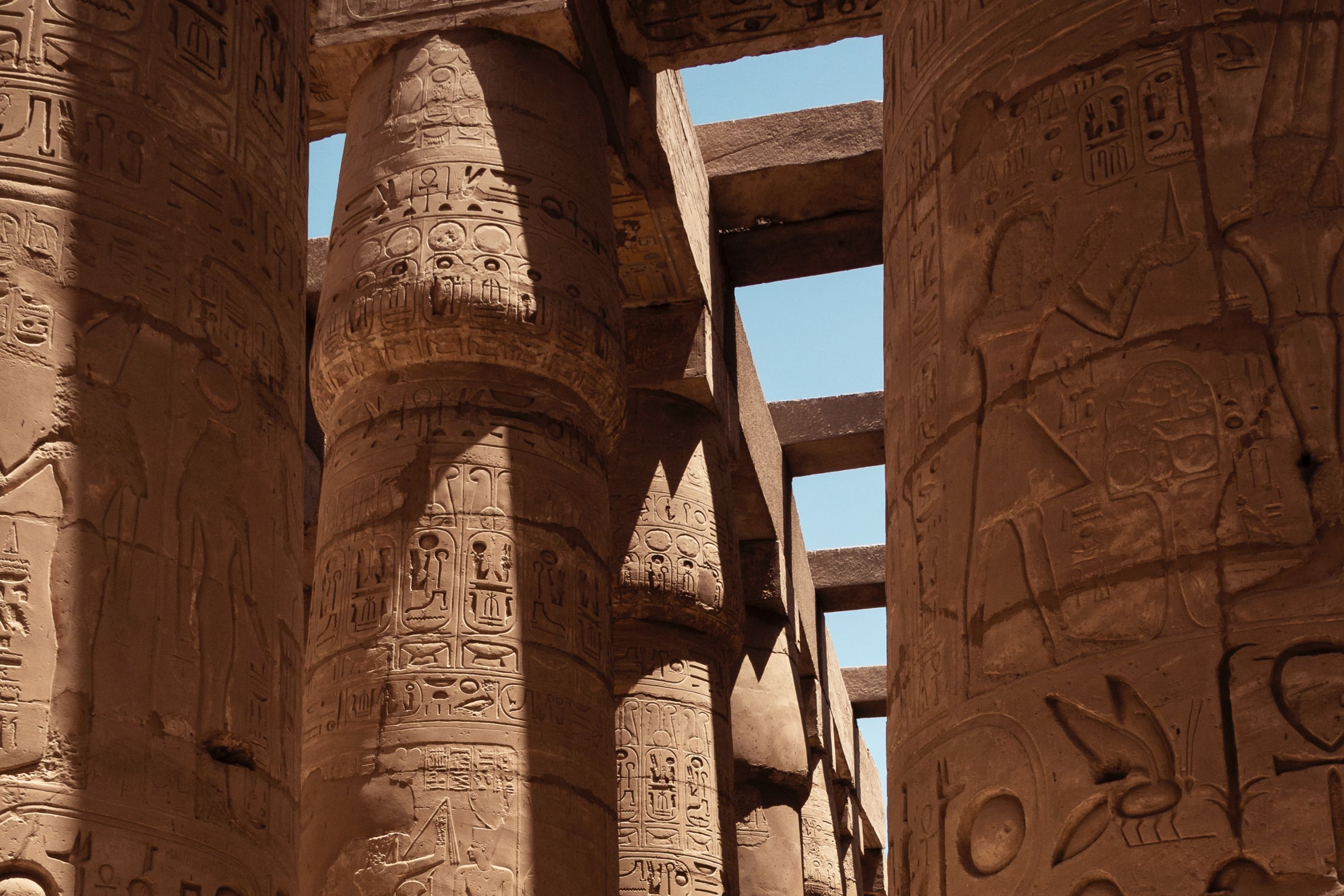Tall columns covered in hieroglyphs with the sky visible above in a temple in Egypt