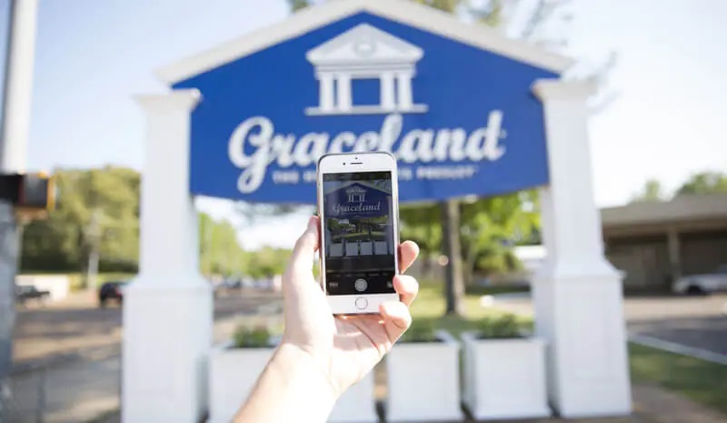 A hand holding a phone taking a picture of Graceland sign