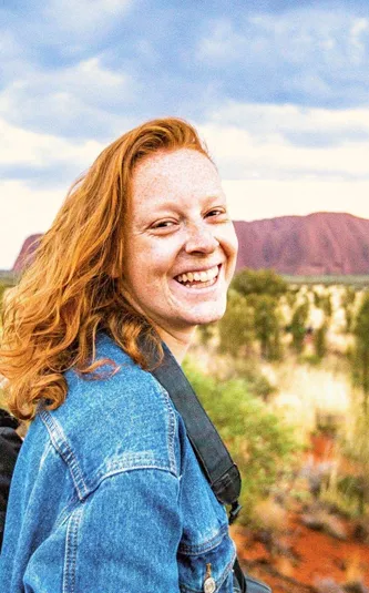 A smiling Contiki traveller takes in the views of Uluru during sunset on the Uluru Explorer tour in Australia's Red Centre