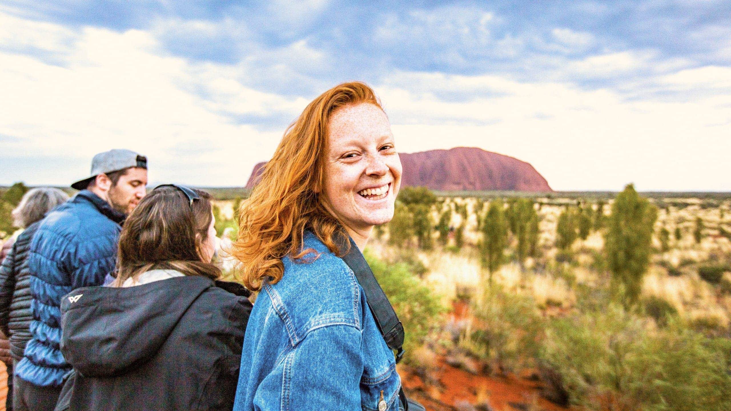 A smiling Contiki traveller takes in the views of Uluru during sunset on the Uluru Explorer tour in Australia's Red Centre