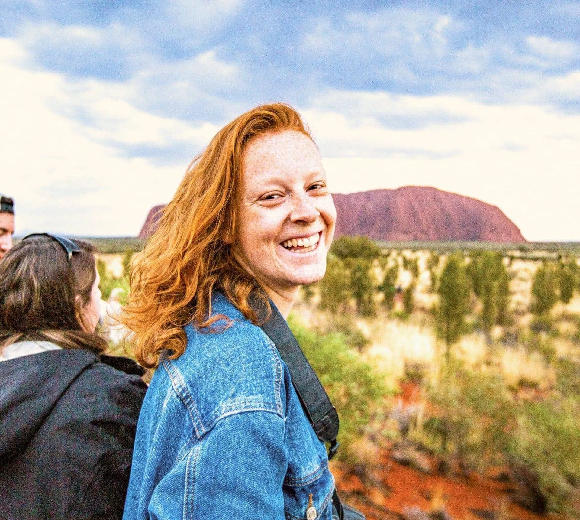 A smiling Contiki traveller takes in the views of Uluru during sunset on the Uluru Explorer tour in Australia's Red Centre