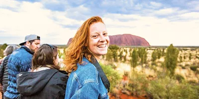 A smiling Contiki traveller takes in the views of Uluru during sunset on the Uluru Explorer tour in Australia's Red Centre