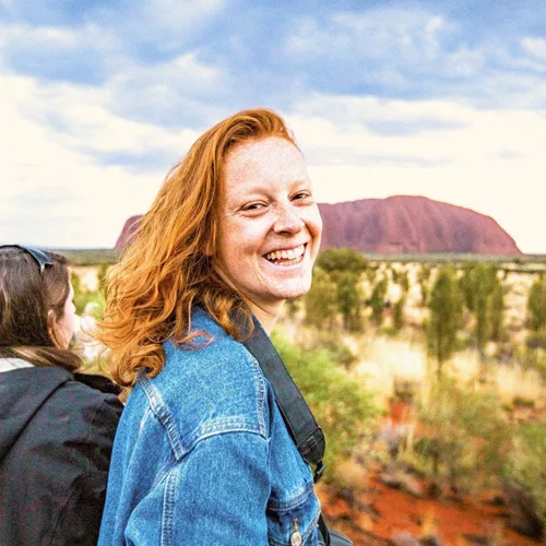 A smiling Contiki traveller takes in the views of Uluru during sunset on the Uluru Explorer tour in Australia's Red Centre