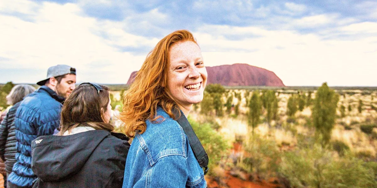 A smiling Contiki traveller takes in the views of Uluru during sunset on the Uluru Explorer tour in Australia's Red Centre