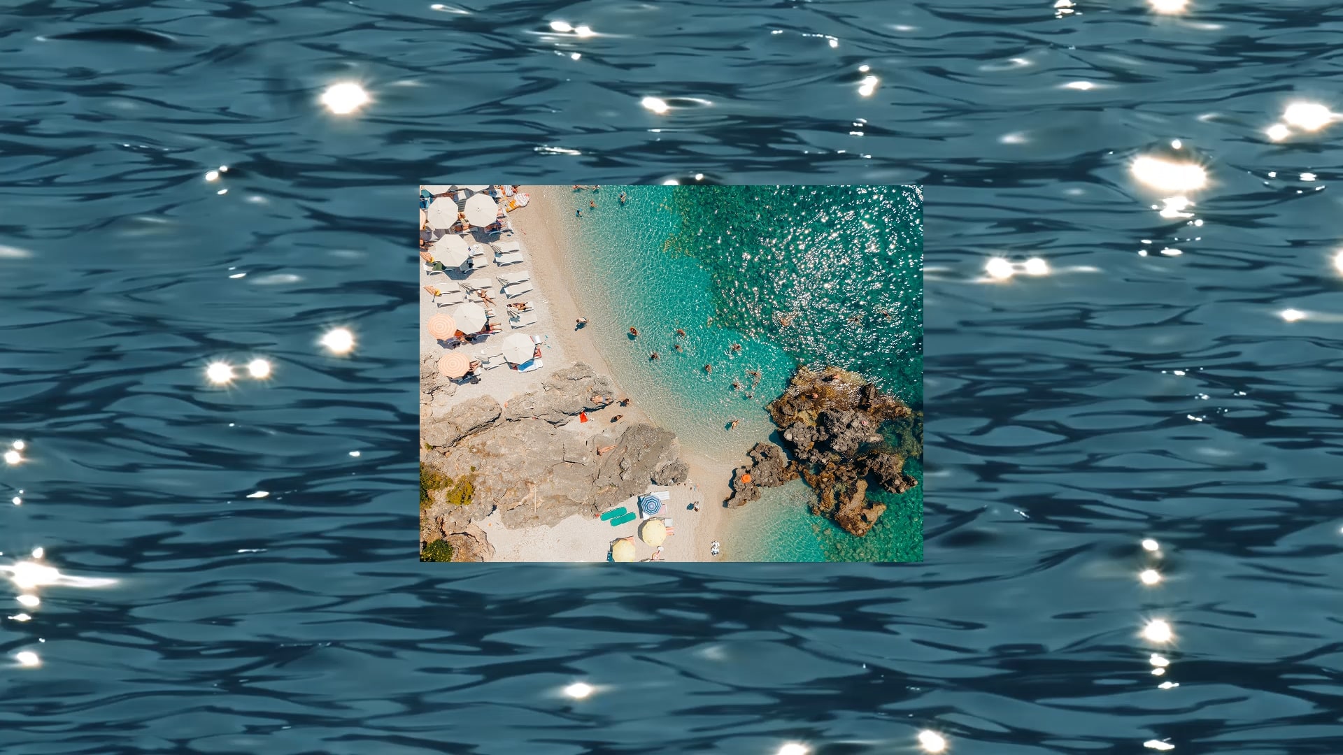 Aerial view of a secluded beach with turquoise water, swimmers, sun umbrellas and rocky coastline on a Contiki Islands trip.
