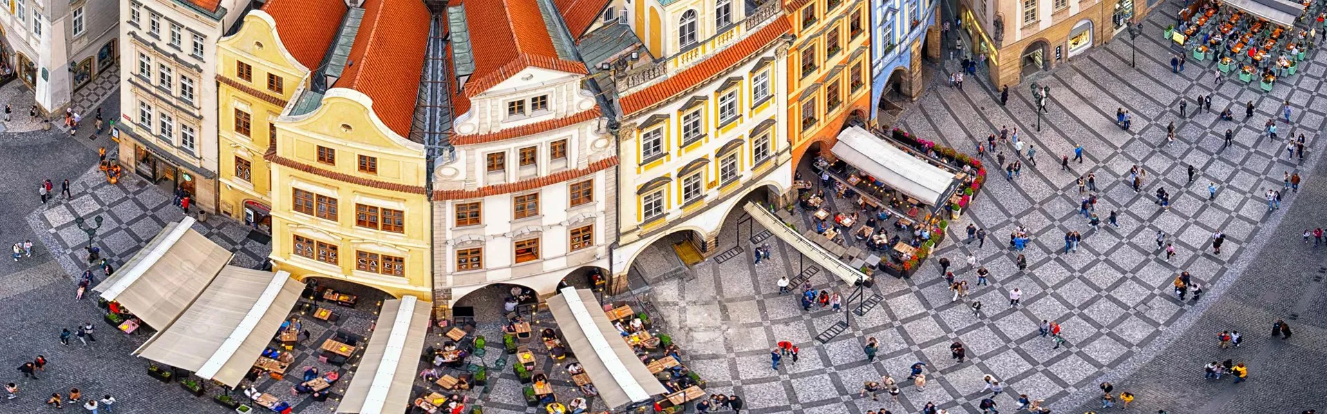 Block of colourful houses on a road with people walking around in Czech.