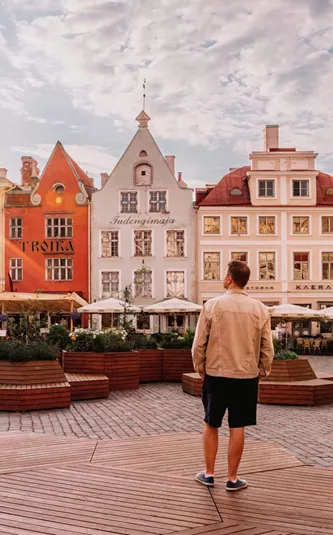 A traveller stands in a cobbled town square surrounded by colourful historic buildings at sunset in Tallinn, Estonia.