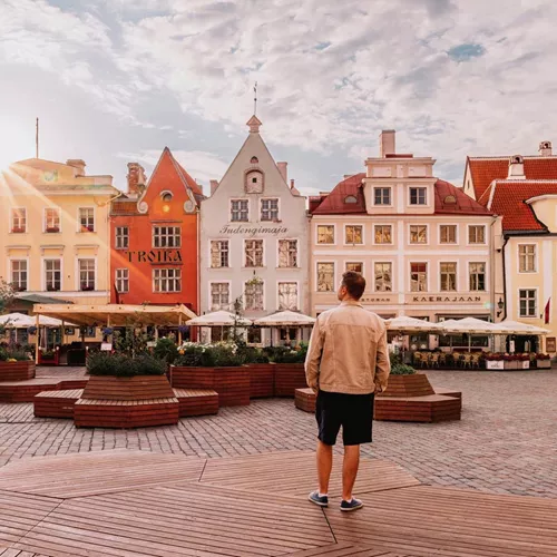 A traveller stands in a cobbled town square surrounded by colourful historic buildings at sunset in Tallinn, Estonia.