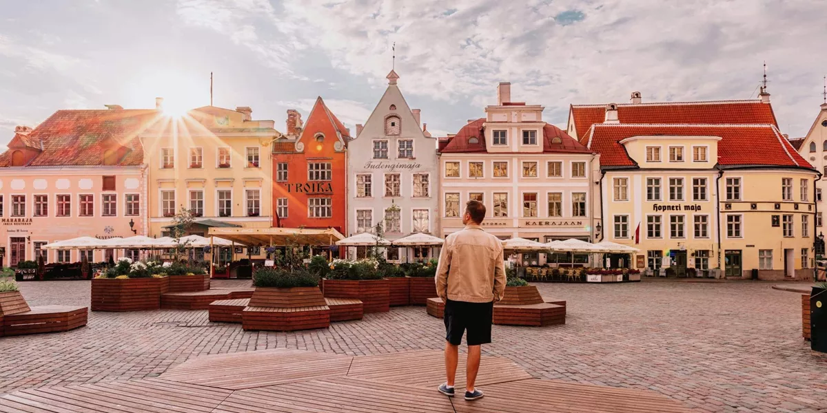 A traveller stands in a cobbled town square surrounded by colourful historic buildings at sunset in Tallinn, Estonia.