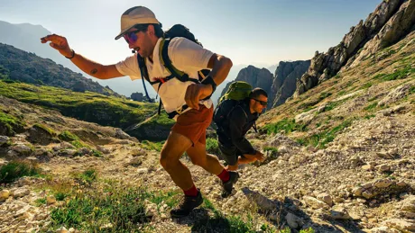Hikers with backpacks climb a rocky trail through the dramatic peaks of the Dolomites, Italy.