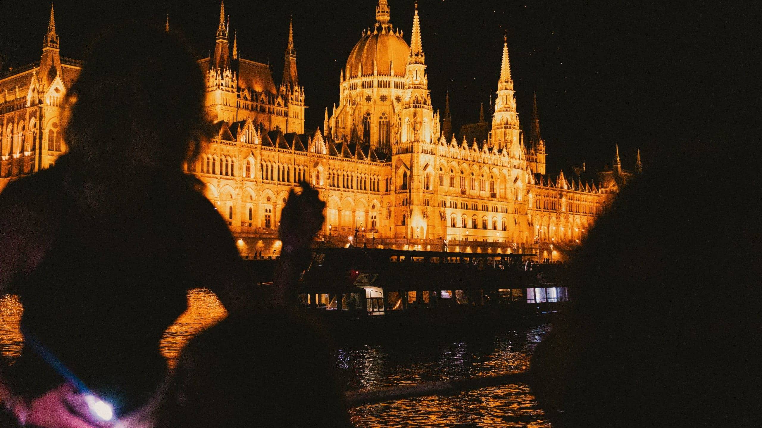 Travellers take in the glowing Hungarian Parliament Building from the Danube River during a night-time sightseeing experience in Budapest - Contiki Berlin to Budapest by Train Tour