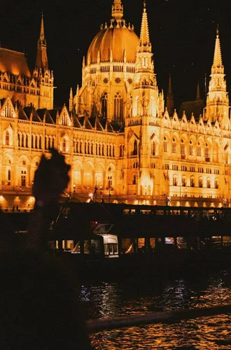 Travellers take in the glowing Hungarian Parliament Building from the Danube River during a night-time sightseeing experience in Budapest - Contiki Berlin to Budapest by Train Tour
