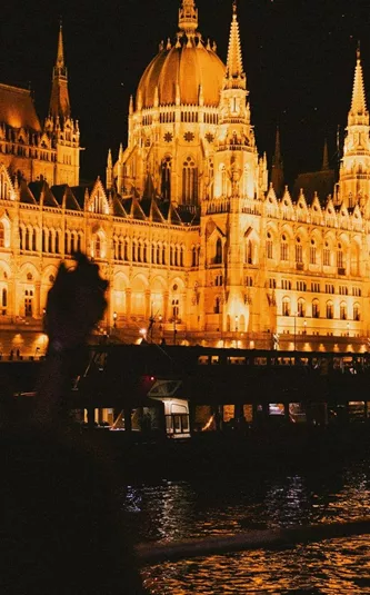 Travellers take in the glowing Hungarian Parliament Building from the Danube River during a night-time sightseeing experience in Budapest - Contiki Berlin to Budapest by Train Tour