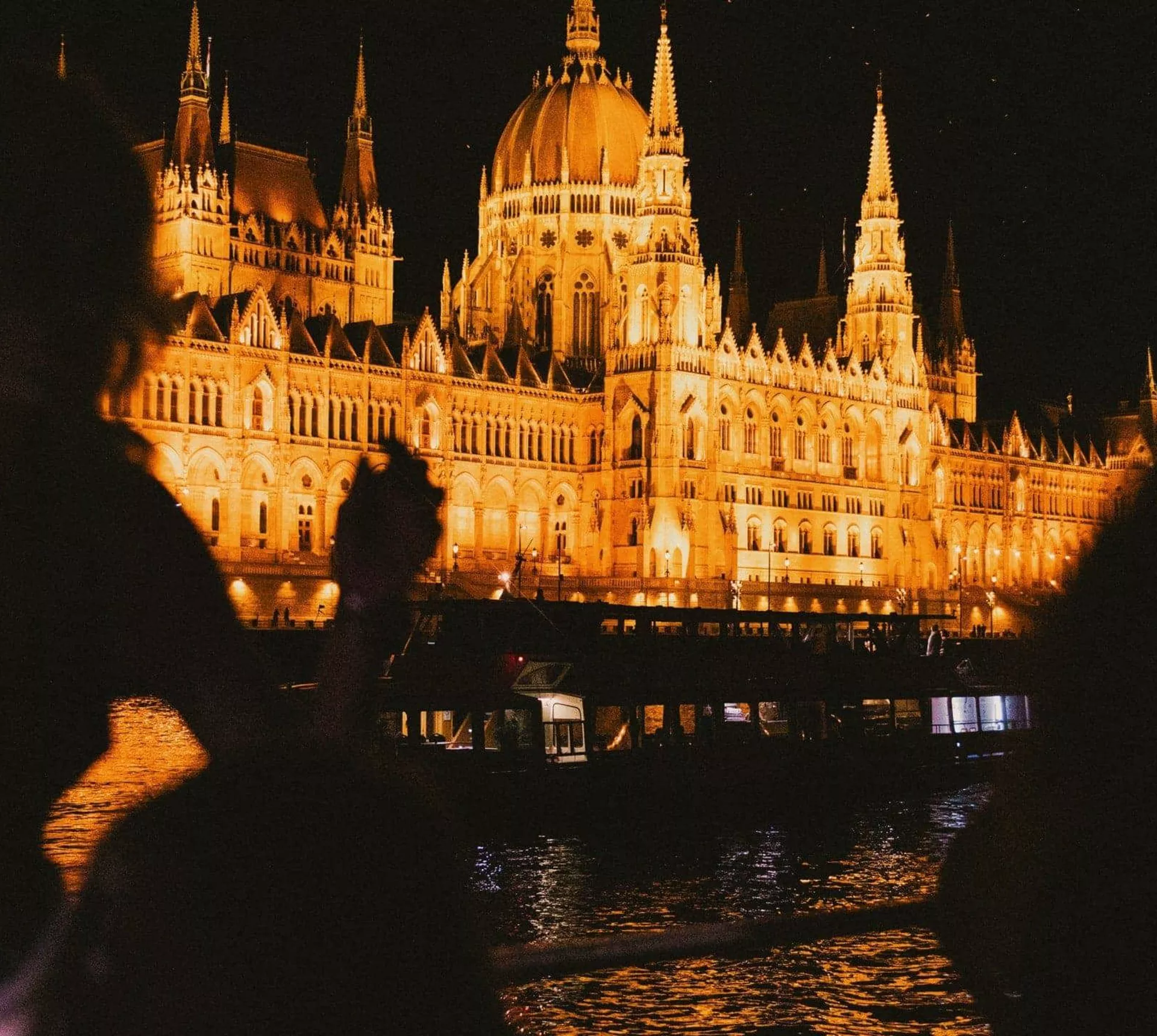 Travellers take in the glowing Hungarian Parliament Building from the Danube River during a night-time sightseeing experience in Budapest - Contiki Berlin to Budapest by Train Tour