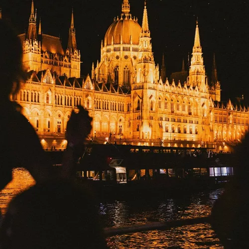 Travellers take in the glowing Hungarian Parliament Building from the Danube River during a night-time sightseeing experience in Budapest - Contiki Berlin to Budapest by Train Tour