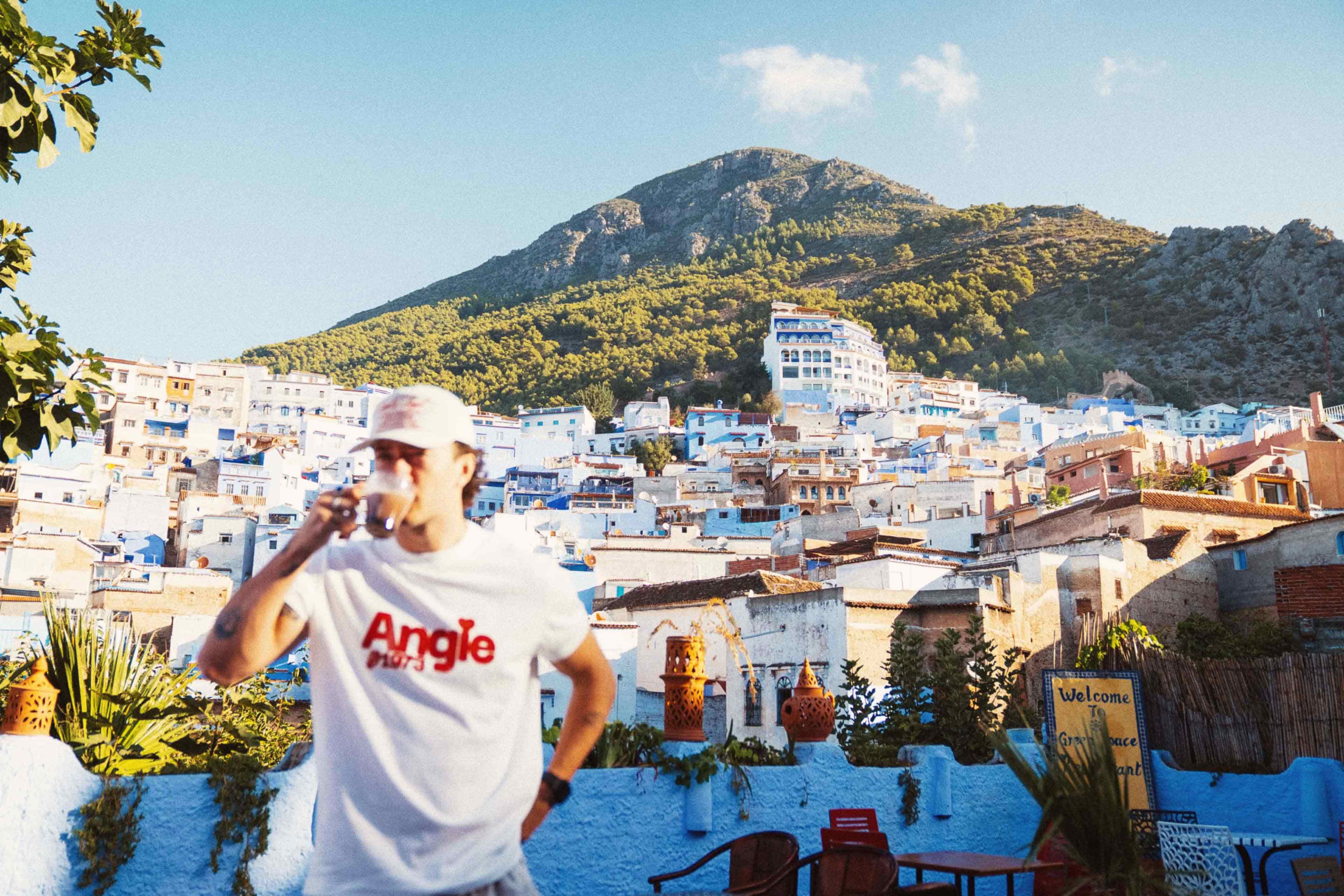 A traveller sips a drink on a rooftop terrace overlooking the blue-washed buildings of Chefchaouen, Morocco.