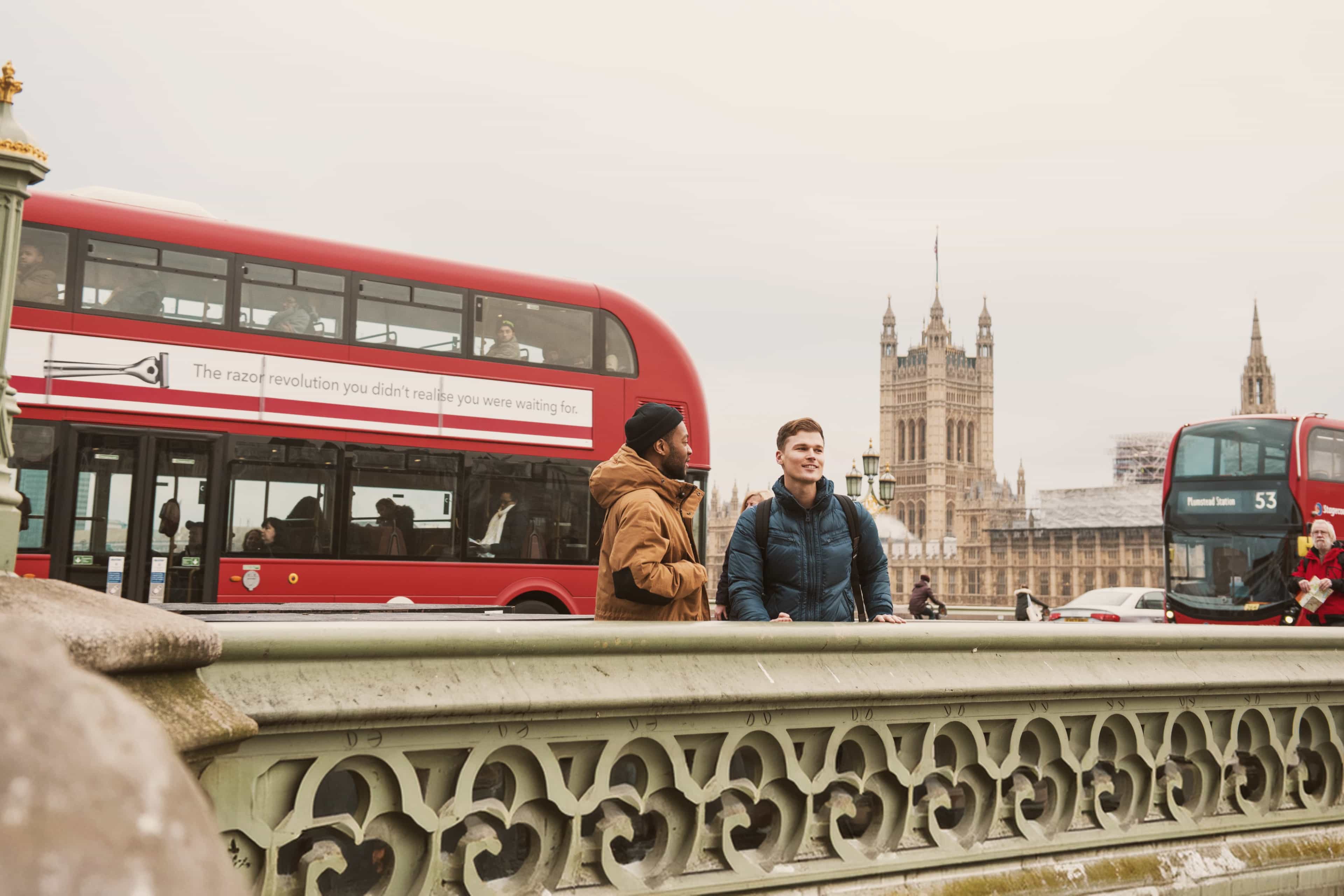 Two travellers chatting on Westminster Bridge with red double-decker buses and the Houses of Parliament behind, London, England