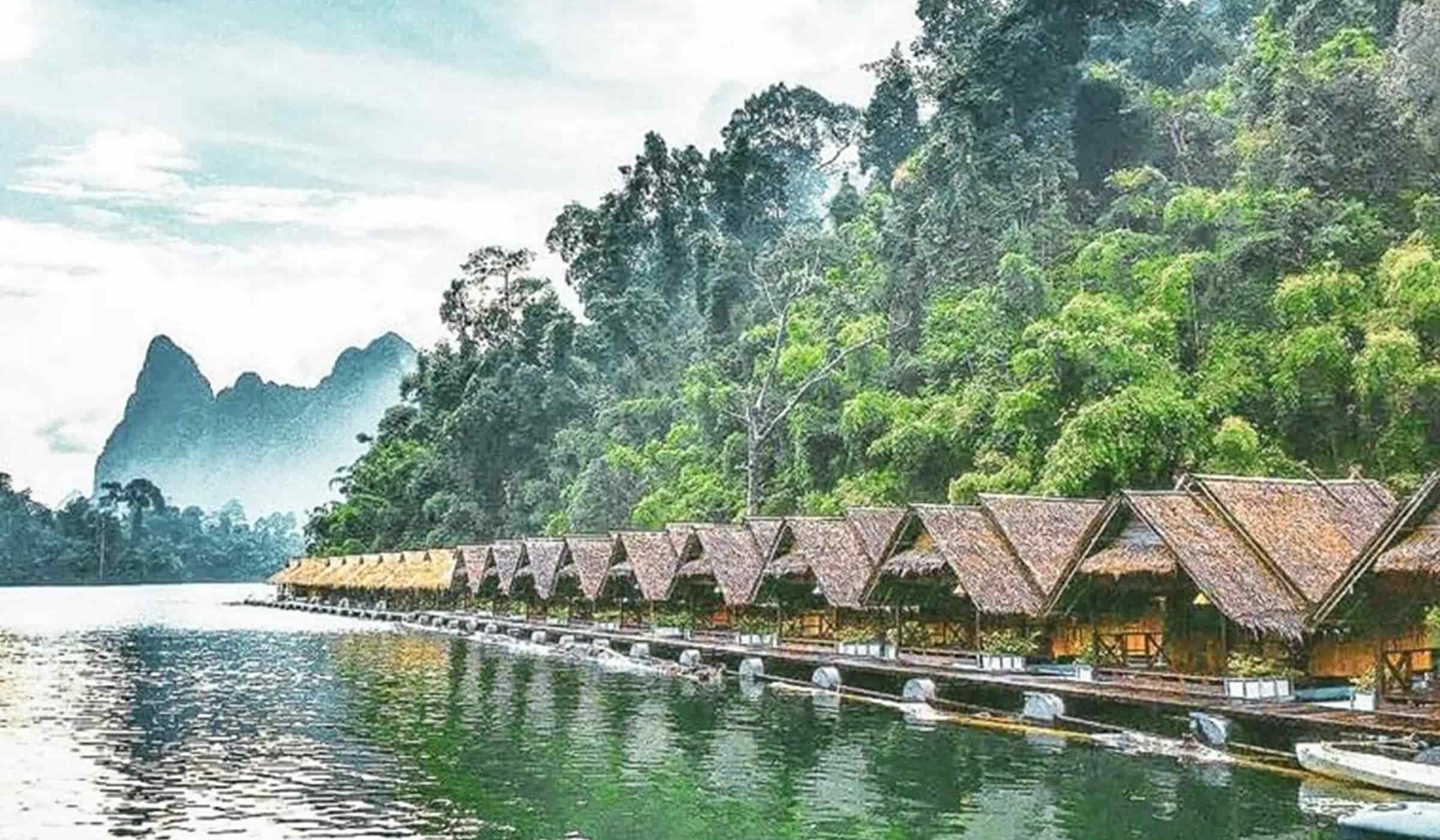 Row of bamboo floating raft bungalows on the River Kwai, surrounded by dense jungle and limestone cliffs, Kanchanaburi, Thailand.