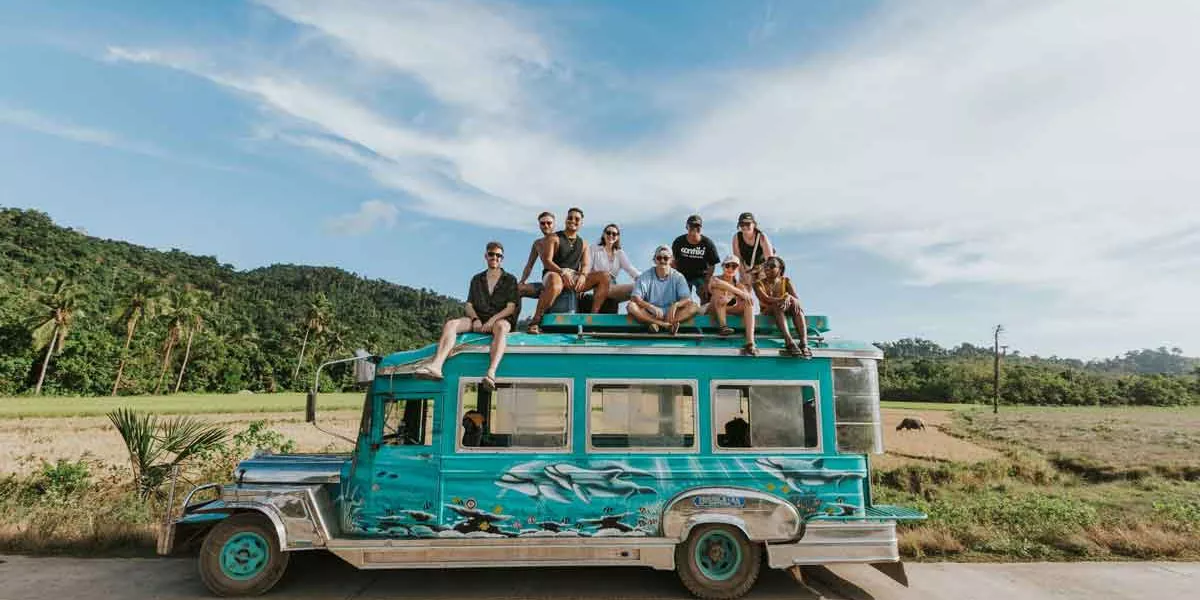 Group Of Young Friends Sitting At The Top Of A Blue Car