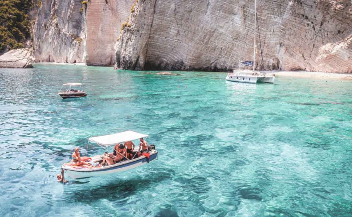 Tourists in a tiny ship floating on clear blue water sea 