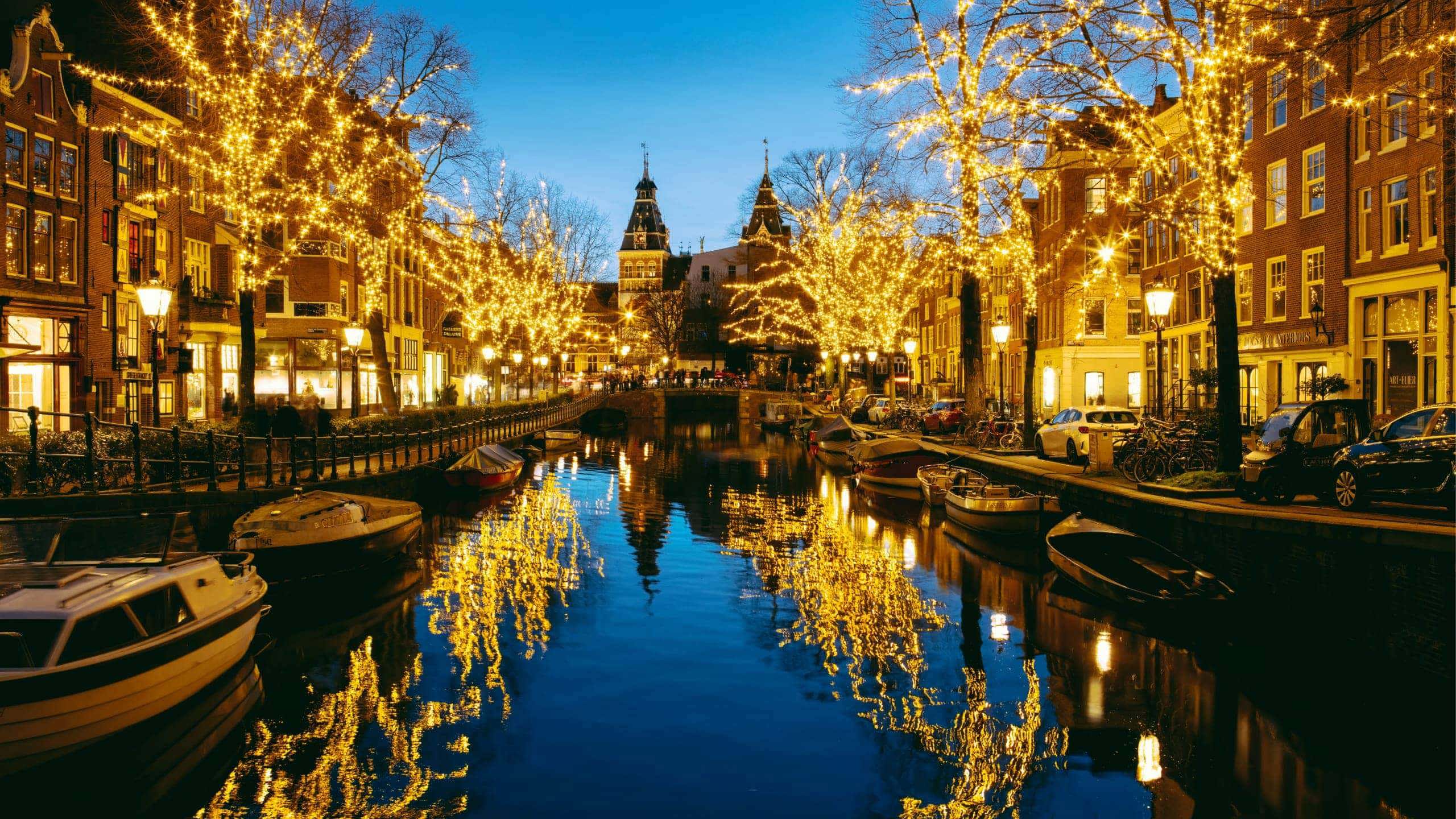 Golden Christmas fairy lights reflecting in an Amsterdam canal at night with the Rijksmuseum in the background - Contiki Netherlands Christmas Tour