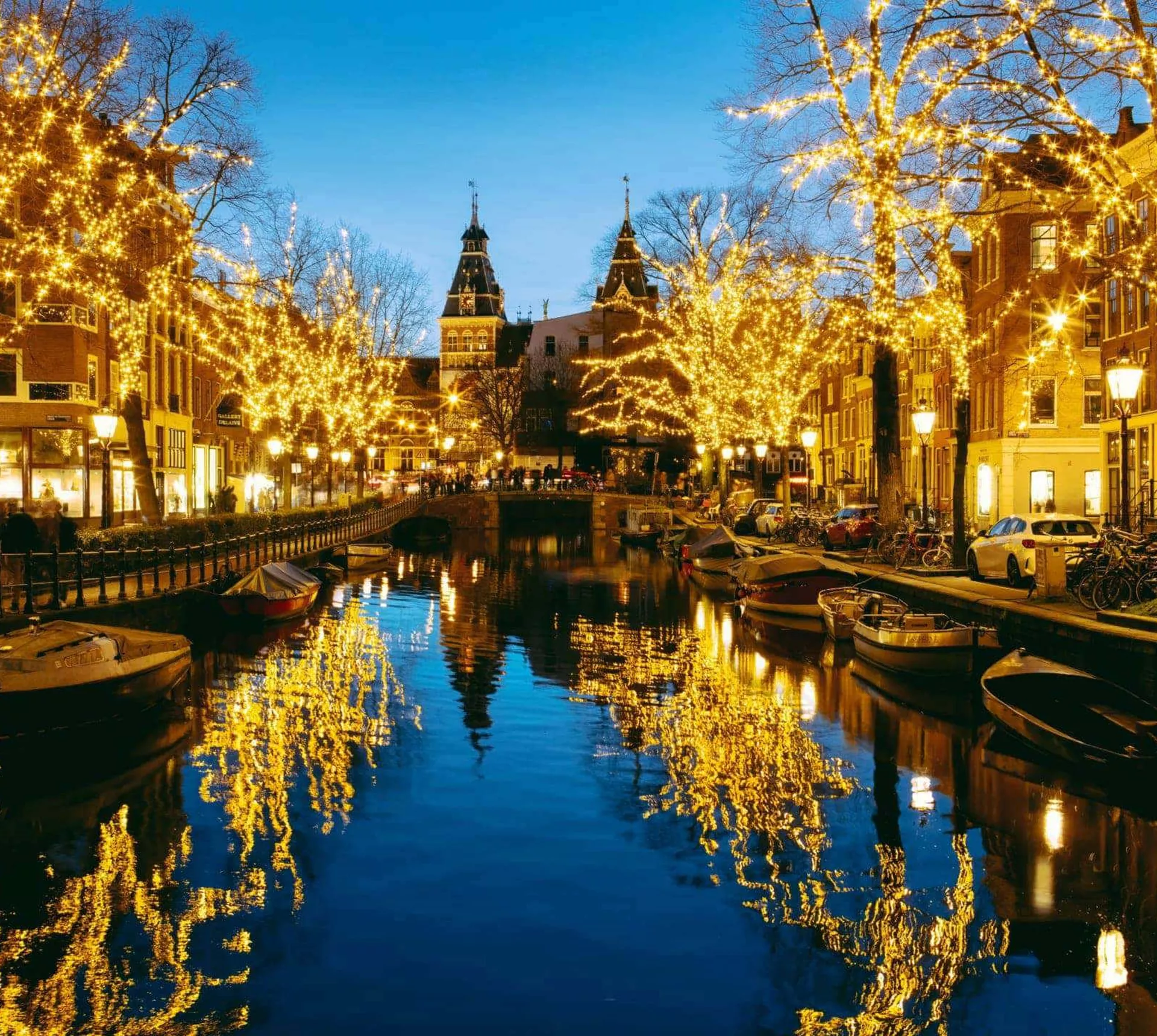 Golden Christmas fairy lights reflecting in an Amsterdam canal at night with the Rijksmuseum in the background - Contiki Netherlands Christmas Tour