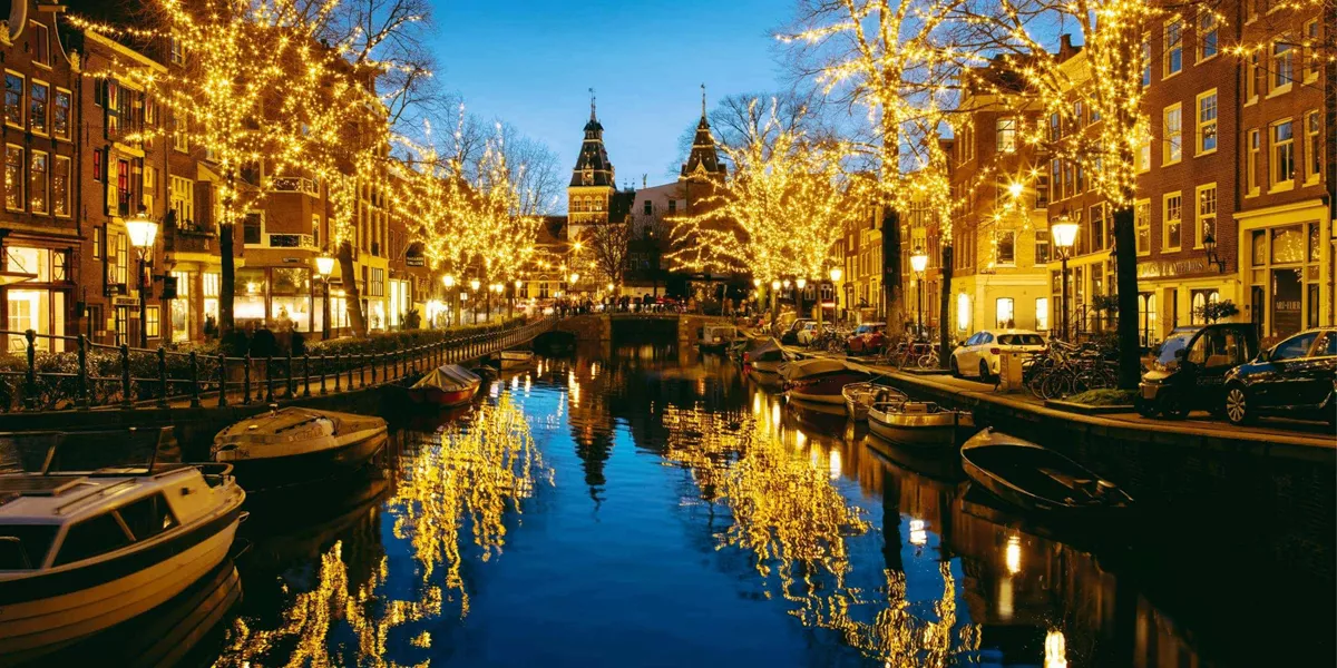 Golden Christmas fairy lights reflecting in an Amsterdam canal at night with the Rijksmuseum in the background - Contiki Netherlands Christmas Tour
