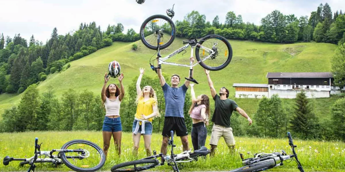 Group Of Young Travelers Throwing Bike In Air Austria