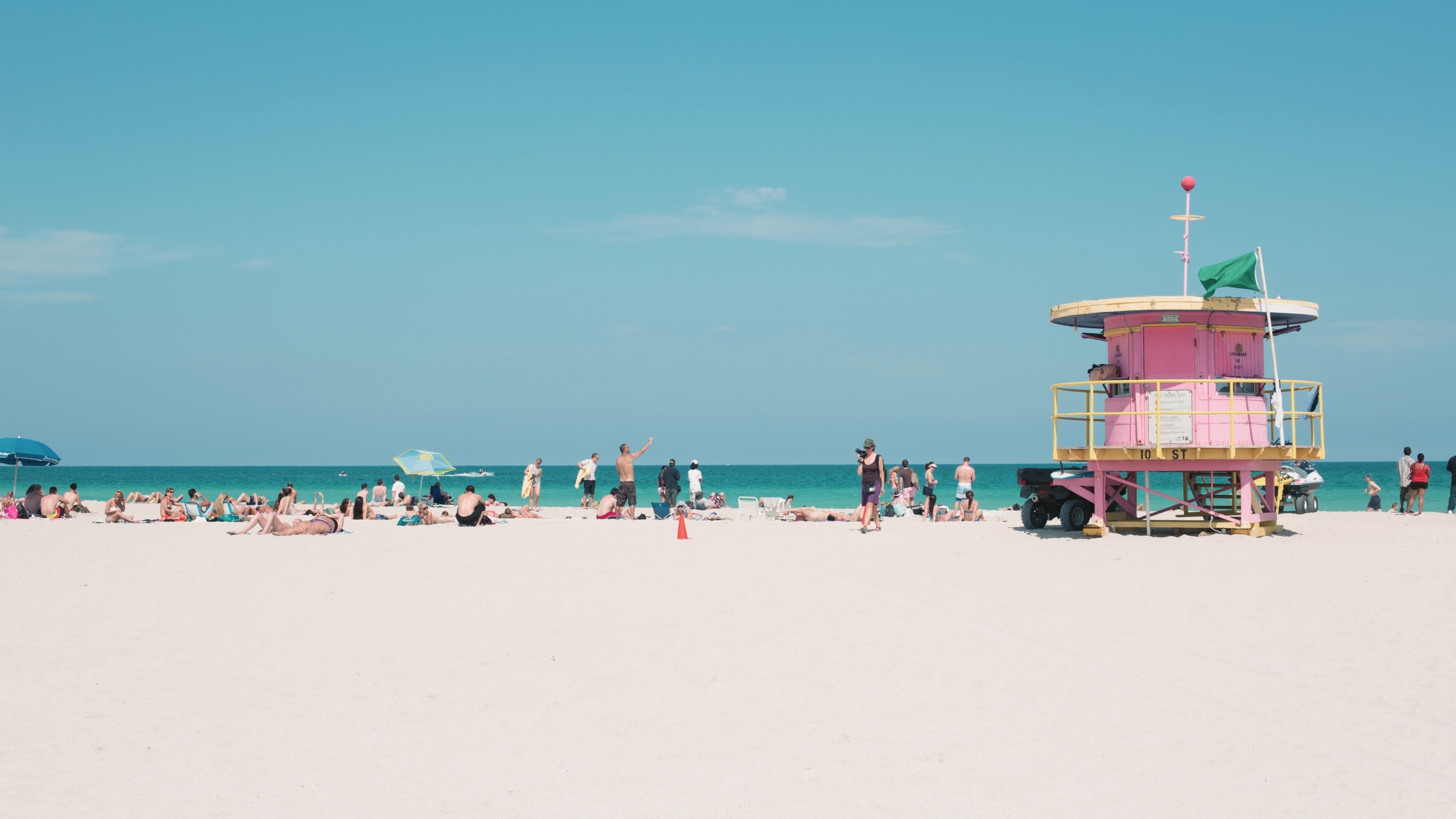 People relaxing on Miami Beach beside the iconic pastel lifeguard tower, enjoying the white sand and turquoise Atlantic Ocean - Contiki Miami to Dallas Tour