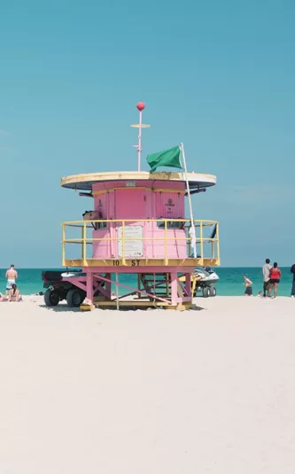 People relaxing on Miami Beach beside the iconic pastel lifeguard tower, enjoying the white sand and turquoise Atlantic Ocean - Contiki Miami to Dallas Tour