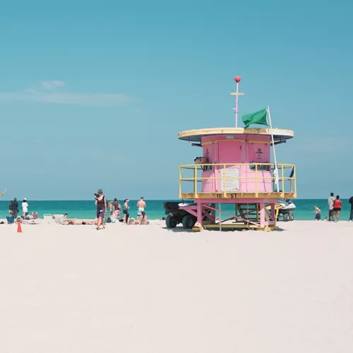 People relaxing on Miami Beach beside the iconic pastel lifeguard tower, enjoying the white sand and turquoise Atlantic Ocean - Contiki Miami to Dallas Tour