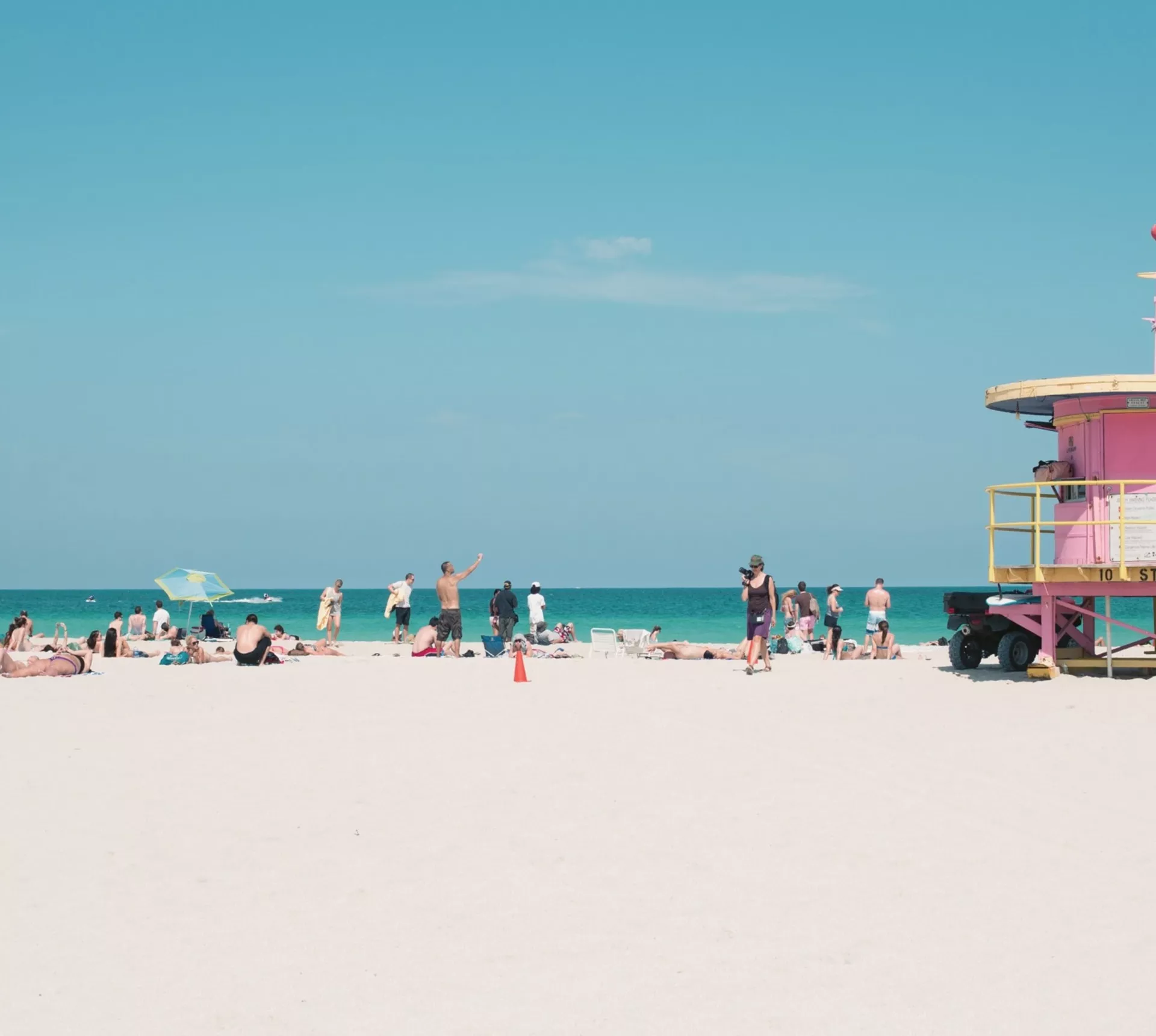 People relaxing on Miami Beach beside the iconic pastel lifeguard tower, enjoying the white sand and turquoise Atlantic Ocean - Contiki Miami to Dallas Tour